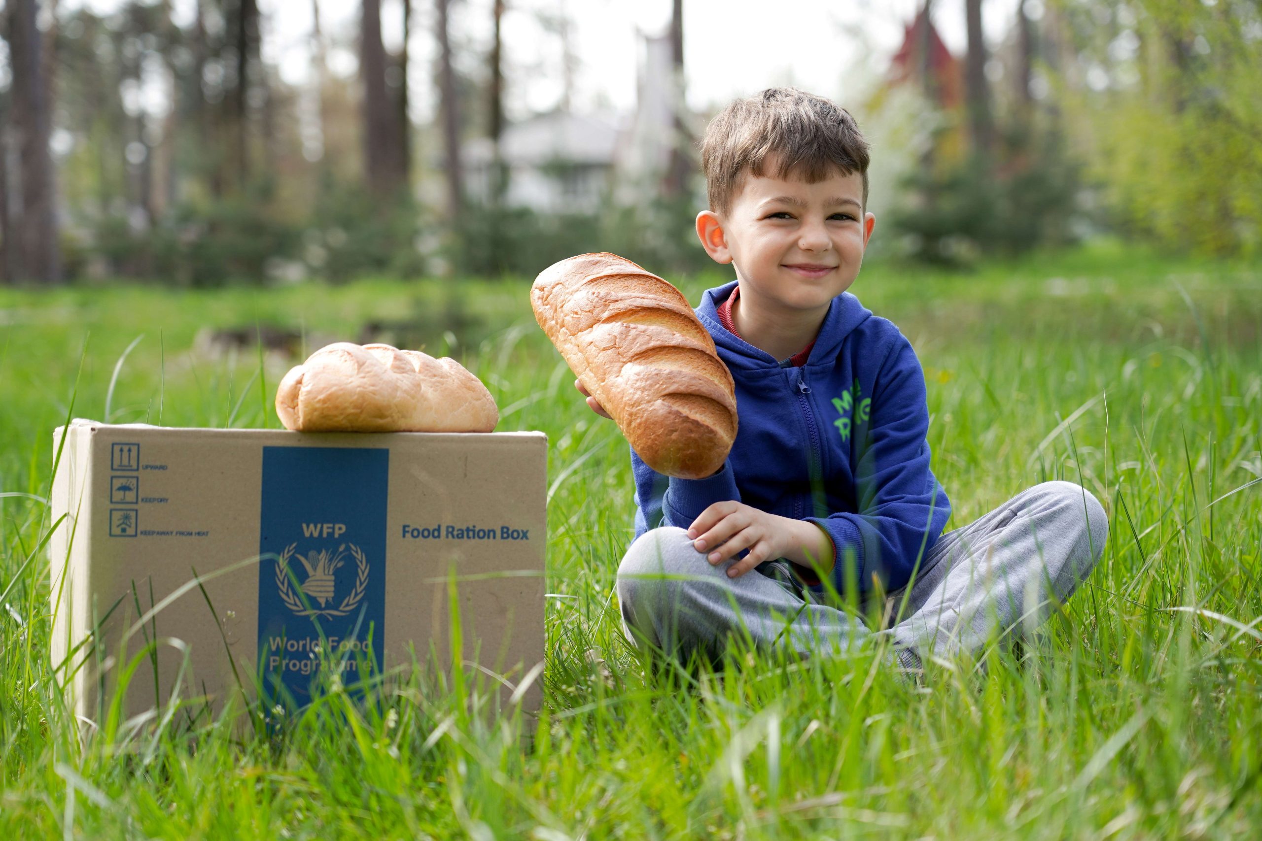 Gutt sitter ved siden av en matpakke fra Verdens matvareprogram og holder et ferskt brød.